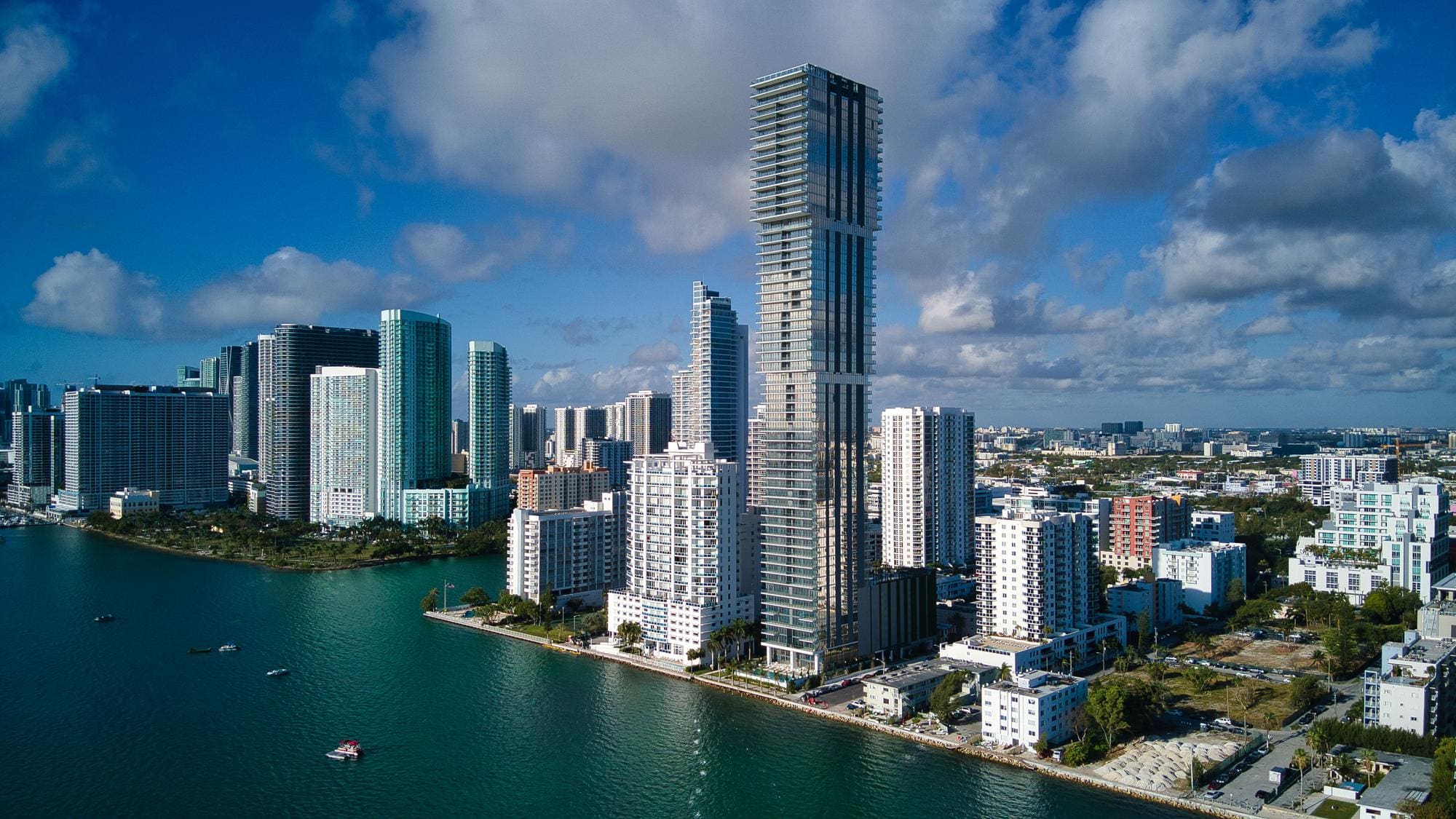 Aerial view of the Miami Edgewater skyline dominated by a tall, slender residential skyscraper, situated on the edge of the blue bay.
